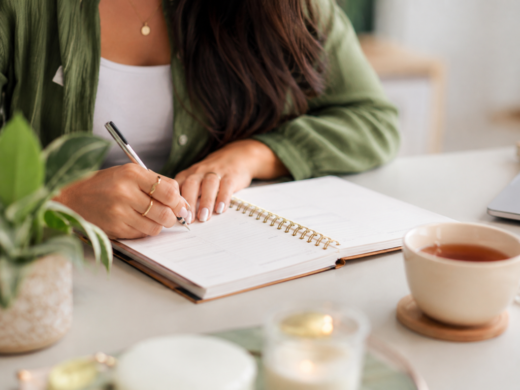 Mulher escrevendo em um planner para organizar metas e pequenos passos, representando planejamento, recomeço e organização da rotina.