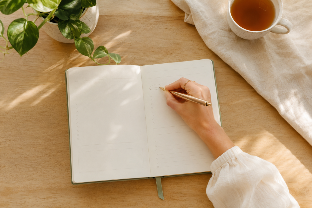 Caderno, chá e planta sobre uma mesa clara representando prioridades e uma vida simples